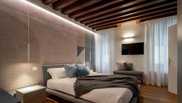 Ein modernes Schlafzimmer mit Bett, Nachttischen, einem Fernseher und einem Fenster mit Vorhängen.