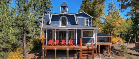 A two-story house with a balcony, a chimney, and a deck with red chairs.