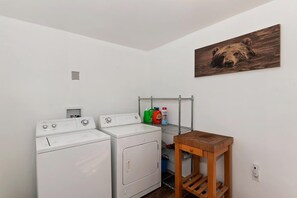 Ein Waschraum mit zwei weißen Waschmaschinen, einem Holztisch und einem Metallregal mit Waschmittelflaschen.