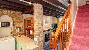 A kitchen with a stone column, wooden cabinets, a microwave, and a fruit bowl. - Jasmine Cottage (Swanage)