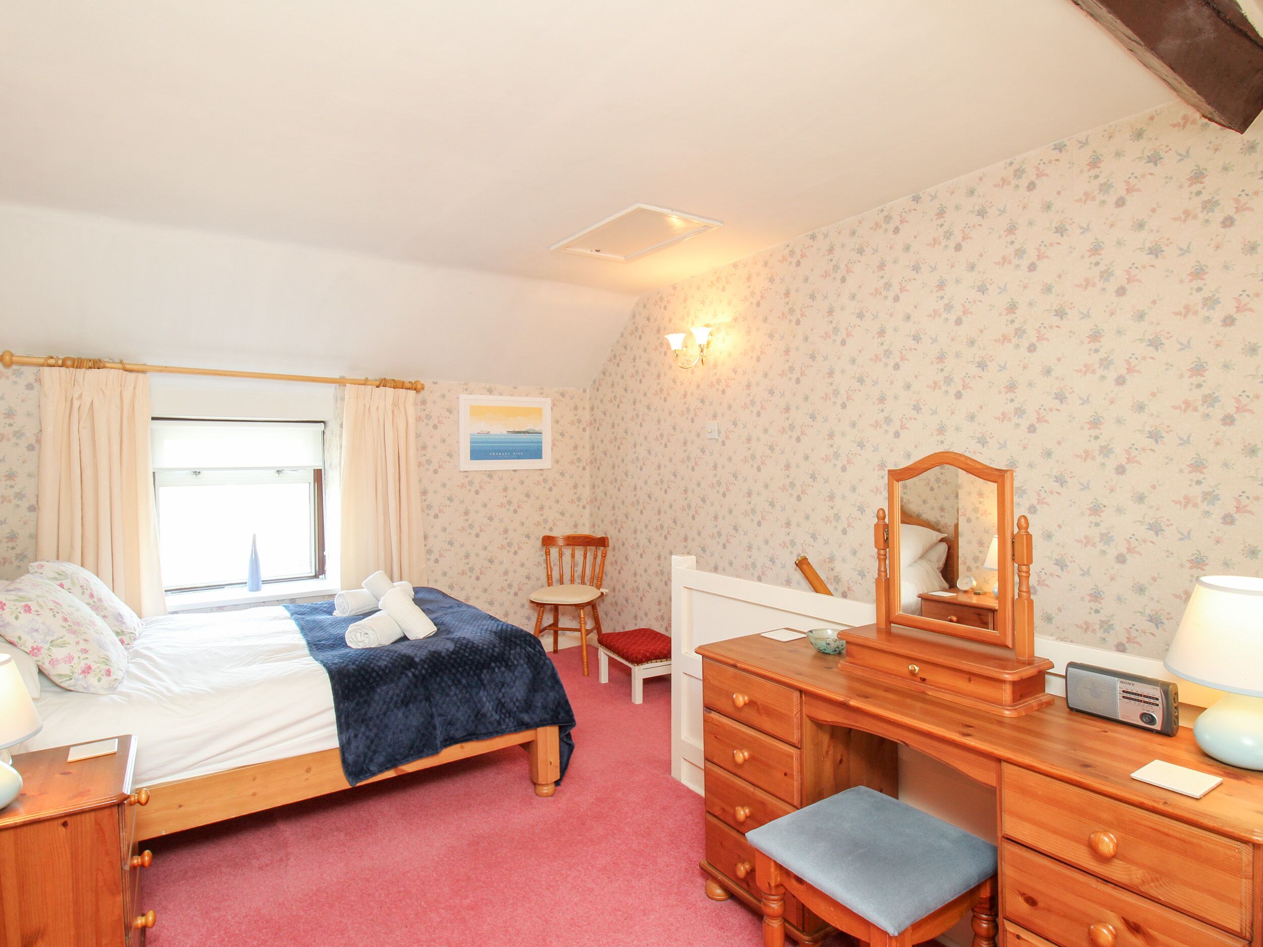 A bedroom with a bed, a wooden dresser, a chair, a desk, and a mirror.