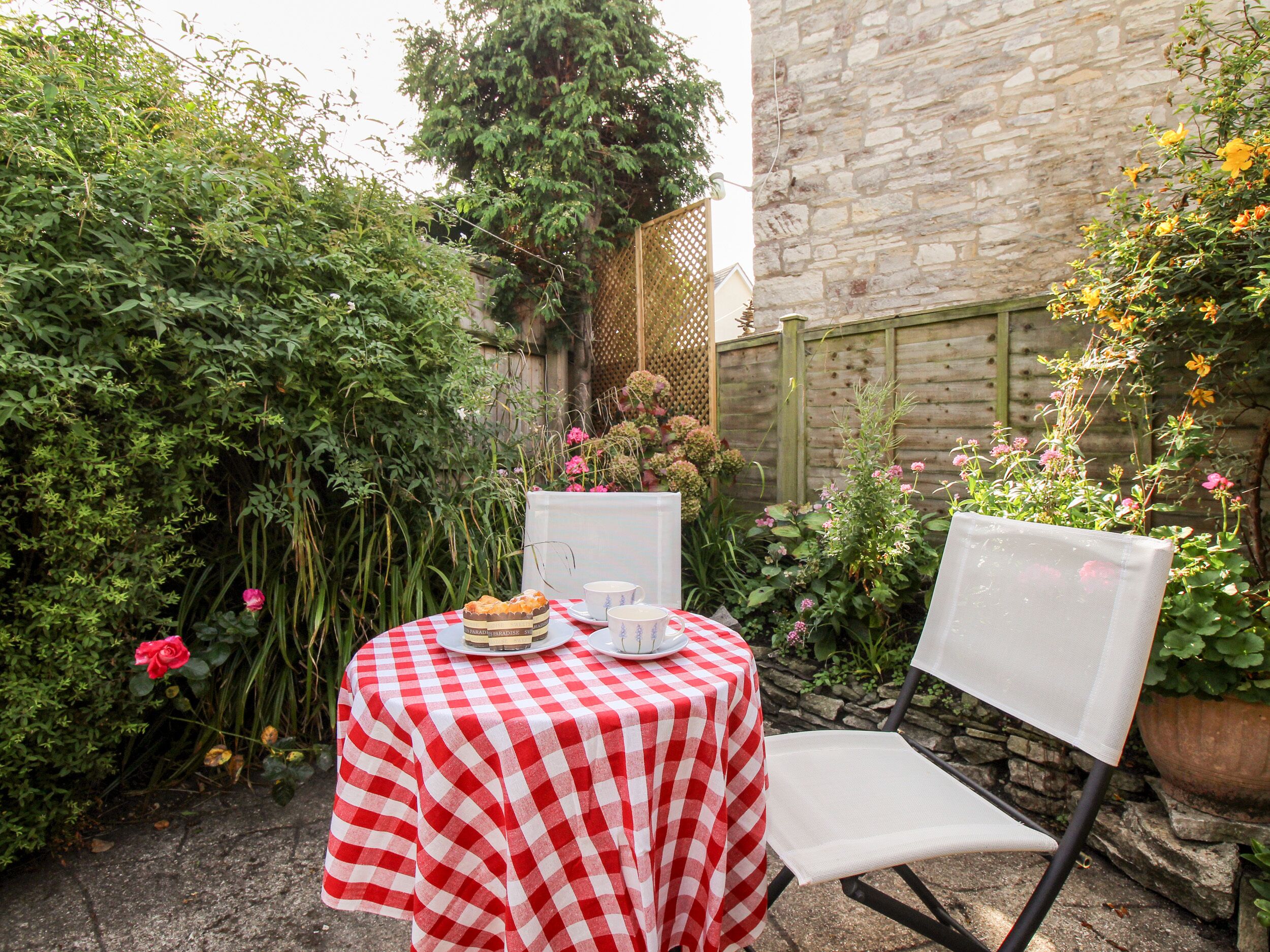 A small outdoor table with a checkered tablecloth, a chair, and a plate with food and cups.
