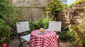 A small outdoor table with a checkered tablecloth, two white chairs, and a plate with a cake and a cup. - Jasmine Cottage (Swanage)