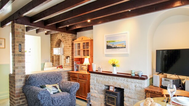 A cozy living room with a fireplace, a sofa, a dining table with plates and a wine glass, and a television. - Jasmine Cottage (Swanage)