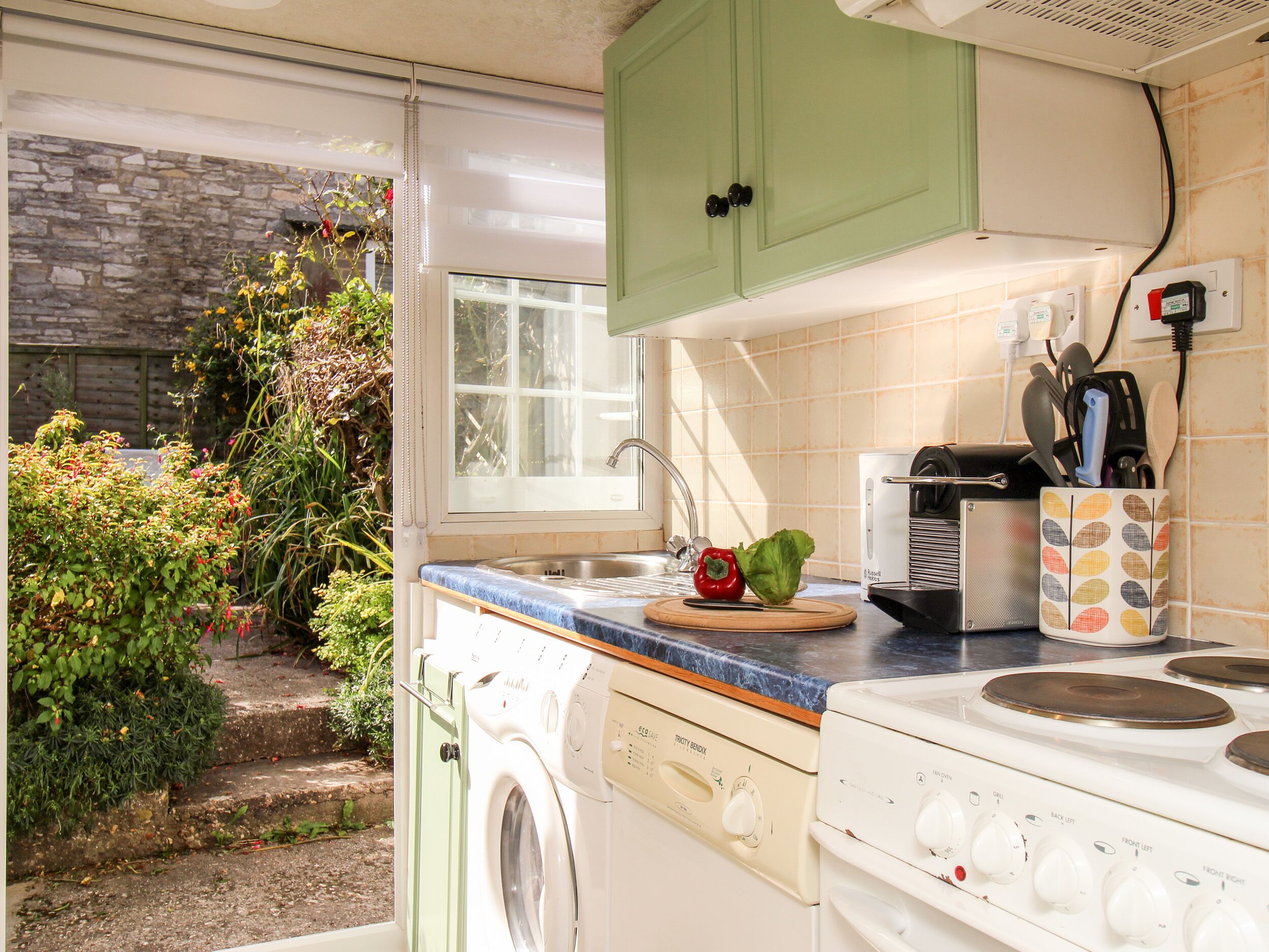 A compact kitchen with a washing machine, a stove, and a window overlooking a garden.