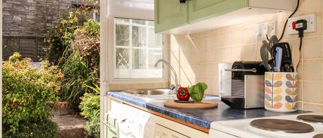 A compact kitchen with a washing machine, a stove, and a window overlooking a garden.