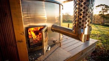 A wood-burning stove with a metal chimney and a wooden bench in front.