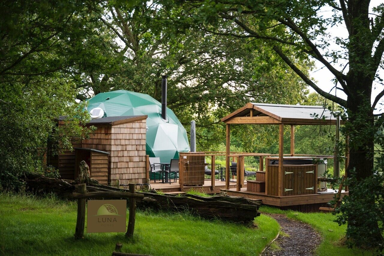 A wooden cabin with a green geodesic dome and a wooden deck with outdoor furniture.