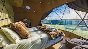 A cozy tented room with a bed, pillows, a blanket, and a view of a snowy landscape. - Luna Domes (Edenbridge)