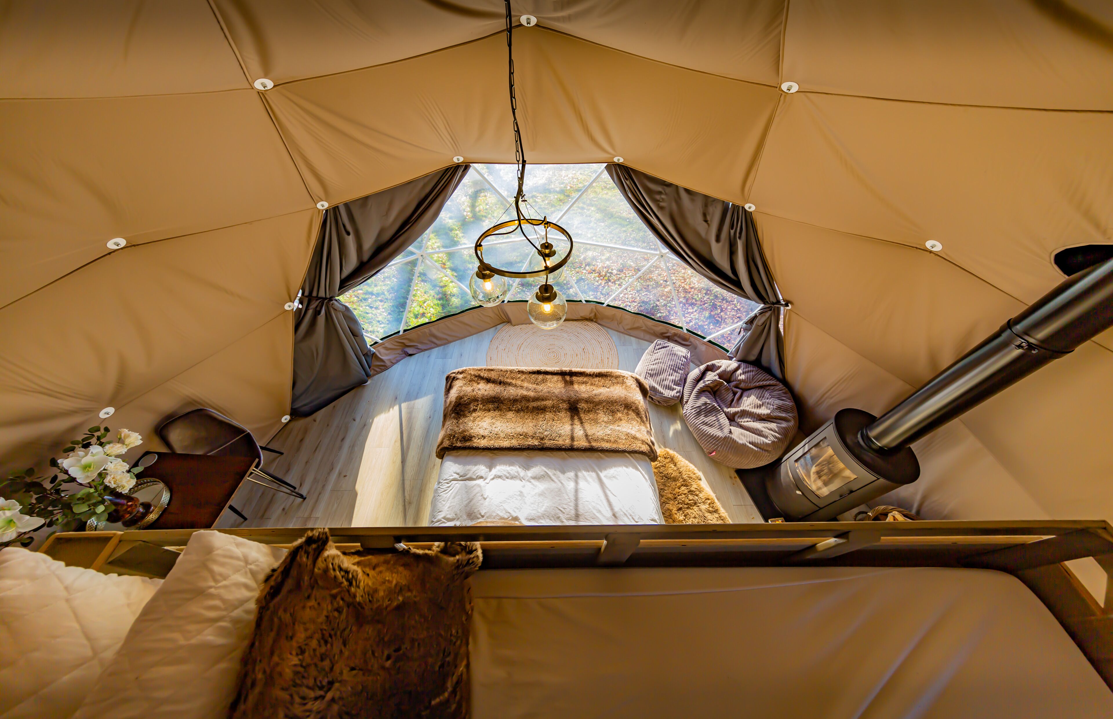 Uma tenda com cama, luminária pendente e aquecedor portátil.