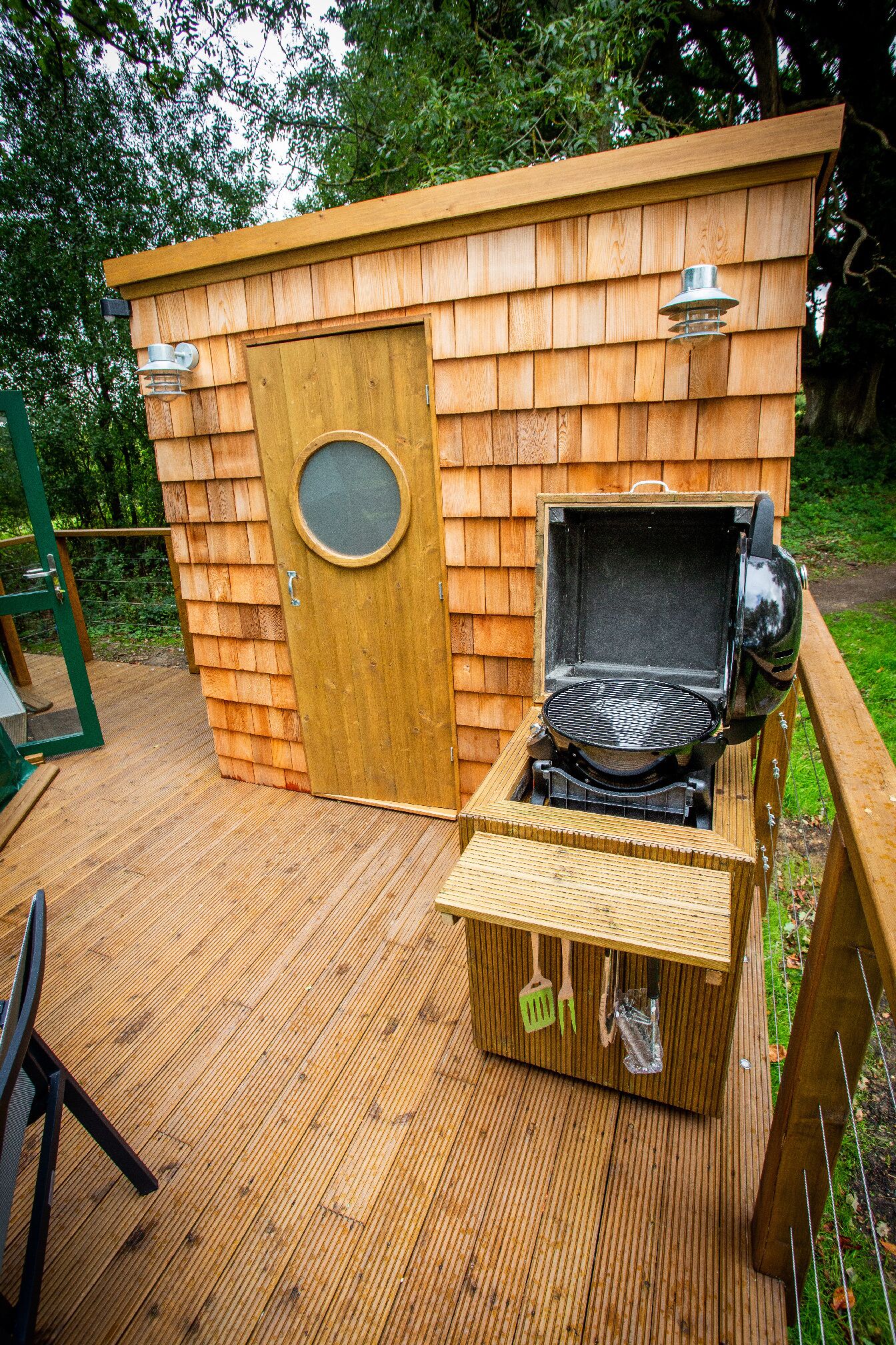 A wooden outdoor grill area with a door and a window, surrounded by a wooden deck.