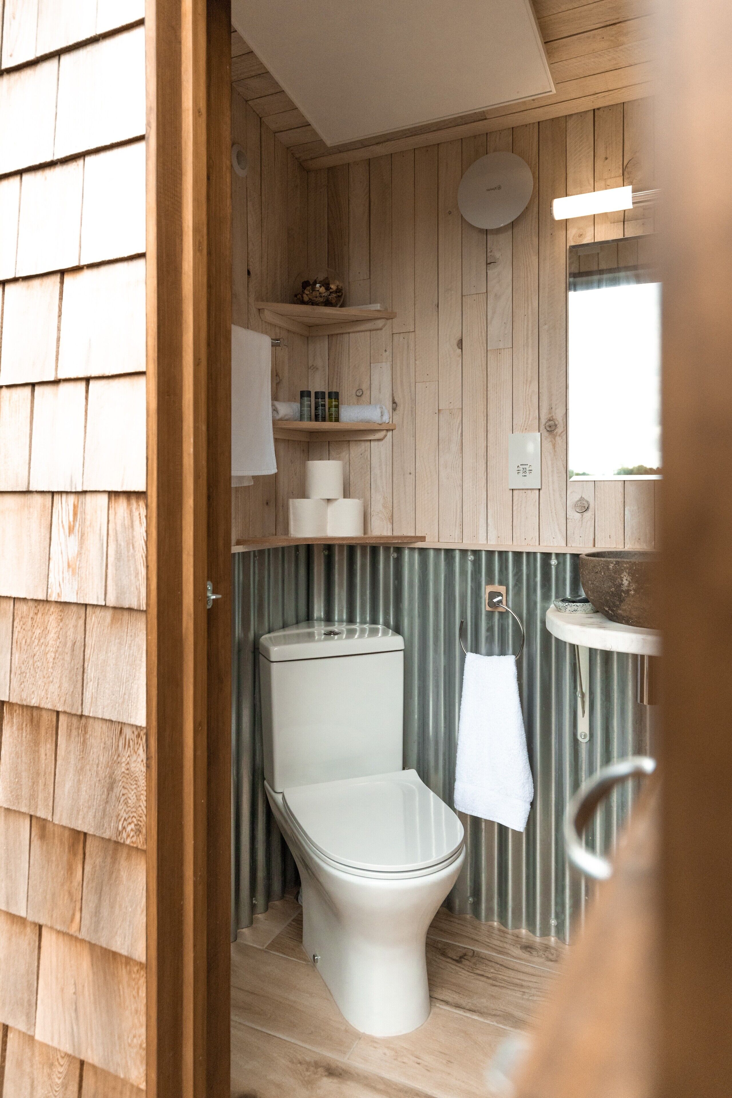 A wooden-paneled bathroom with a toilet, a sink, and a mirror.
