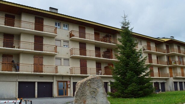 A multi-story hotel with balconies, a stone wall, and a large rock in the foreground.