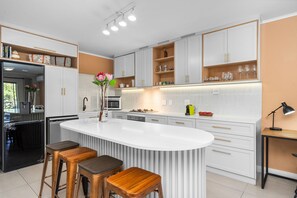 A modern kitchen with white cabinetry, a central island with stools, and a built-in oven. - Mayfair Luxury 212 (Cape Town)