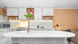 A modern kitchen with white cabinetry, a central island with stools, and a vase with flowers. - Mayfair Luxury 212 (Cape Town)