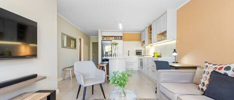 A modern living room with a sofa, a coffee table, a TV, and a kitchen in the background.