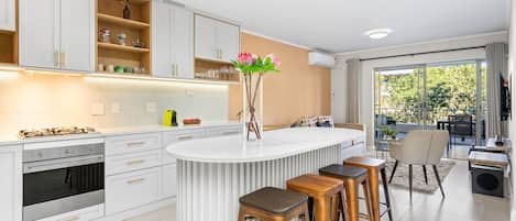 Una cocina moderna con armarios blancos, una isla central con taburetes y vistas a un balcón exterior.