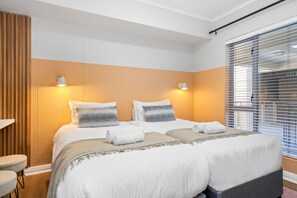 Ett hotellrum med två sängar, en väggpanel i trä och ett fönster med persienner.