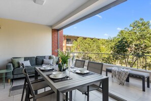 A balcony with a dining table set for two, a sofa, and a bench. - Mayfair Luxury 212 (Cape Town)