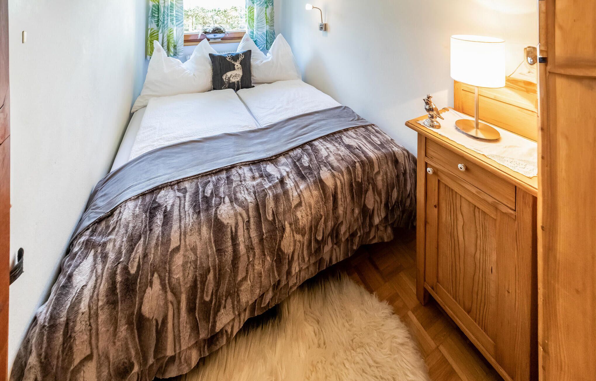 A small bedroom with a bed, a nightstand, a lamp, and a wooden cabinet.