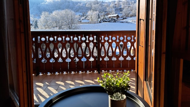 A balcony with a view of a snowy landscape, a wooden fence, and a potted plant on a table. - Charming apartment in Morillon, near cable car (Morillon Village)