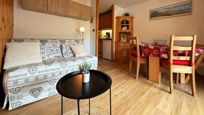 A cozy living room with a patterned sofa, a small round table, and a dining area with a red tablecloth. - Charming apartment in Morillon, near cable car (Morillon Village)