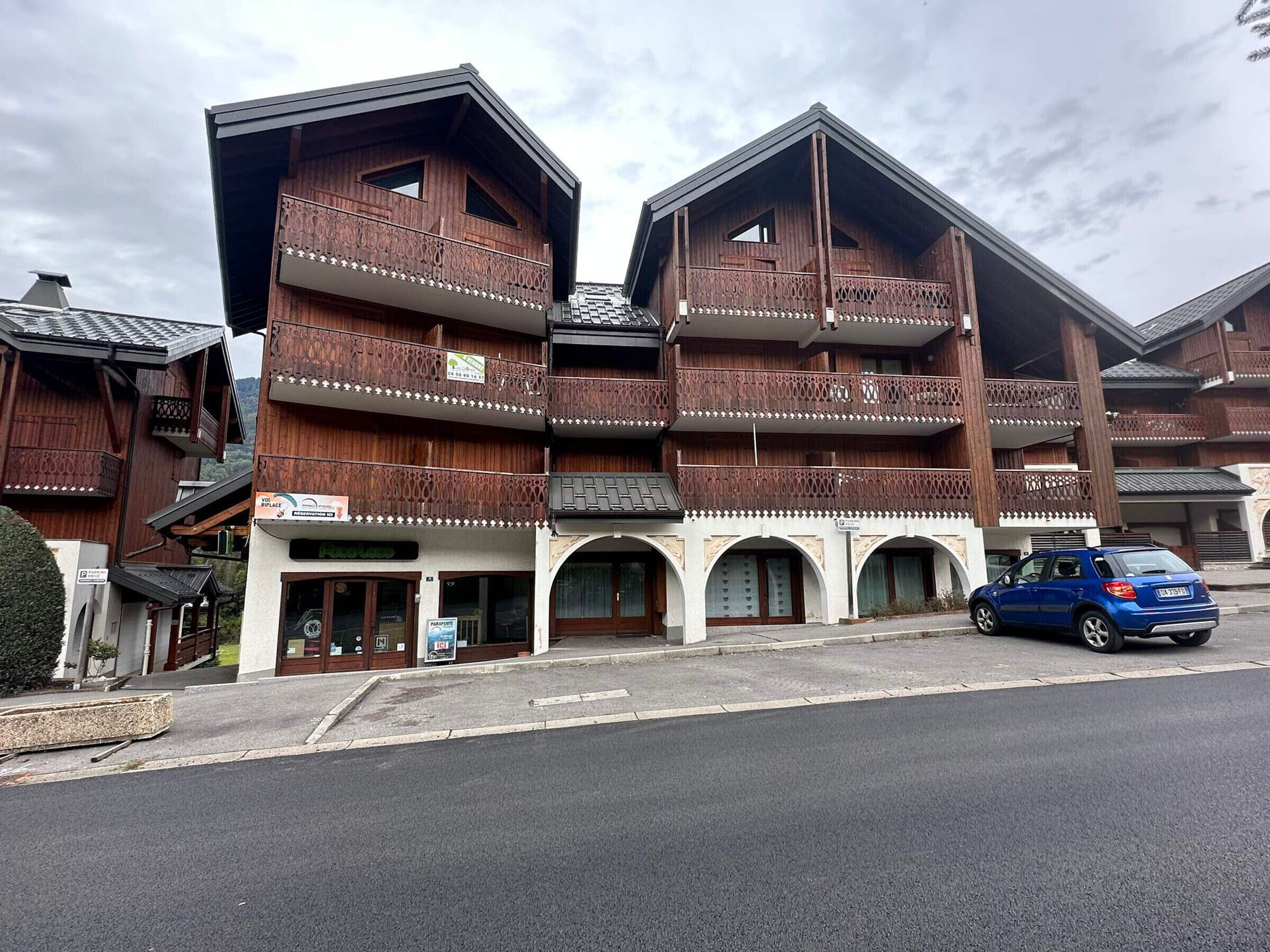 Un bâtiment en bois doté de balcons, une enseigne indiquant «Hôtel», et une voiture bleue garée devant.