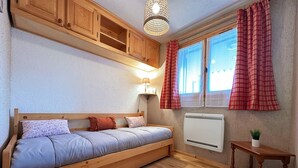 A cozy bedroom with a single bed, wooden cabinets, a small table, and a radiator. - Charming apartment in Morillon, near cable car (Morillon Village)