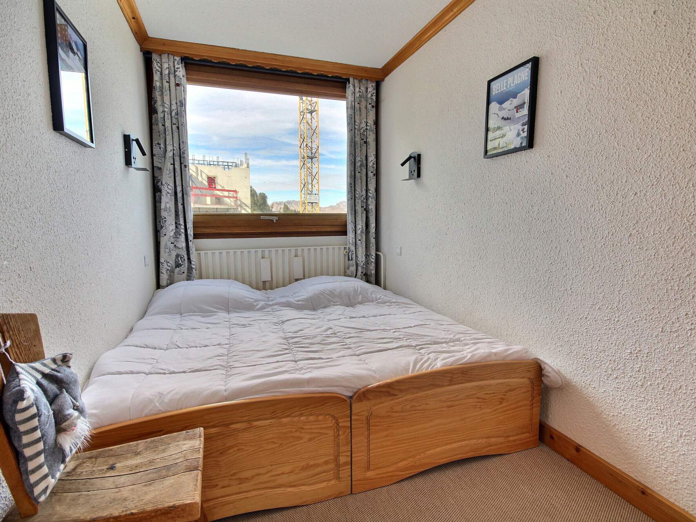 Une chambre à coucher avec un lit en bois, une fenêtre avec des rideaux, un radiateur et un tableau accroché au mur.