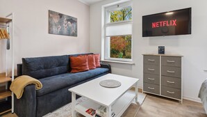 Una sala de estar moderna con un sofá azul, una mesa de centro blanca, un televisor en la pared y una ventana con persianas.