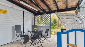 Un área de estar al aire libre con techo, una mesa, sillas, una pared blanca y techo de madera.