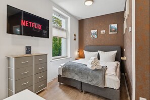 Un dormitorio moderno con una cama, un televisor montado en la pared, una ventana y un aparador.