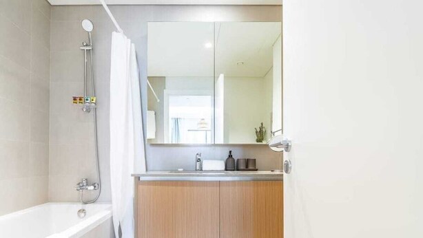 A modern bathroom with a bathtub, a shower, a vanity with a mirror, and a toilet. - Dubai Creek Gem, Stylish Condo With Two Balconies (Dubai)
