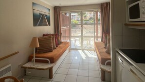 Een compacte hotelkamer met een bank, een klein tafeltje, een lamp, een magnetron en uitzicht op het balkon.