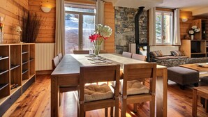 Un intérieur en bois comprenant une table à manger, des chaises, une cheminée en pierre et un coin salon confortable.