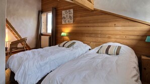 Une chambre avec deux lits, des poutres en bois, un radiateur, une lampe et une fenêtre.