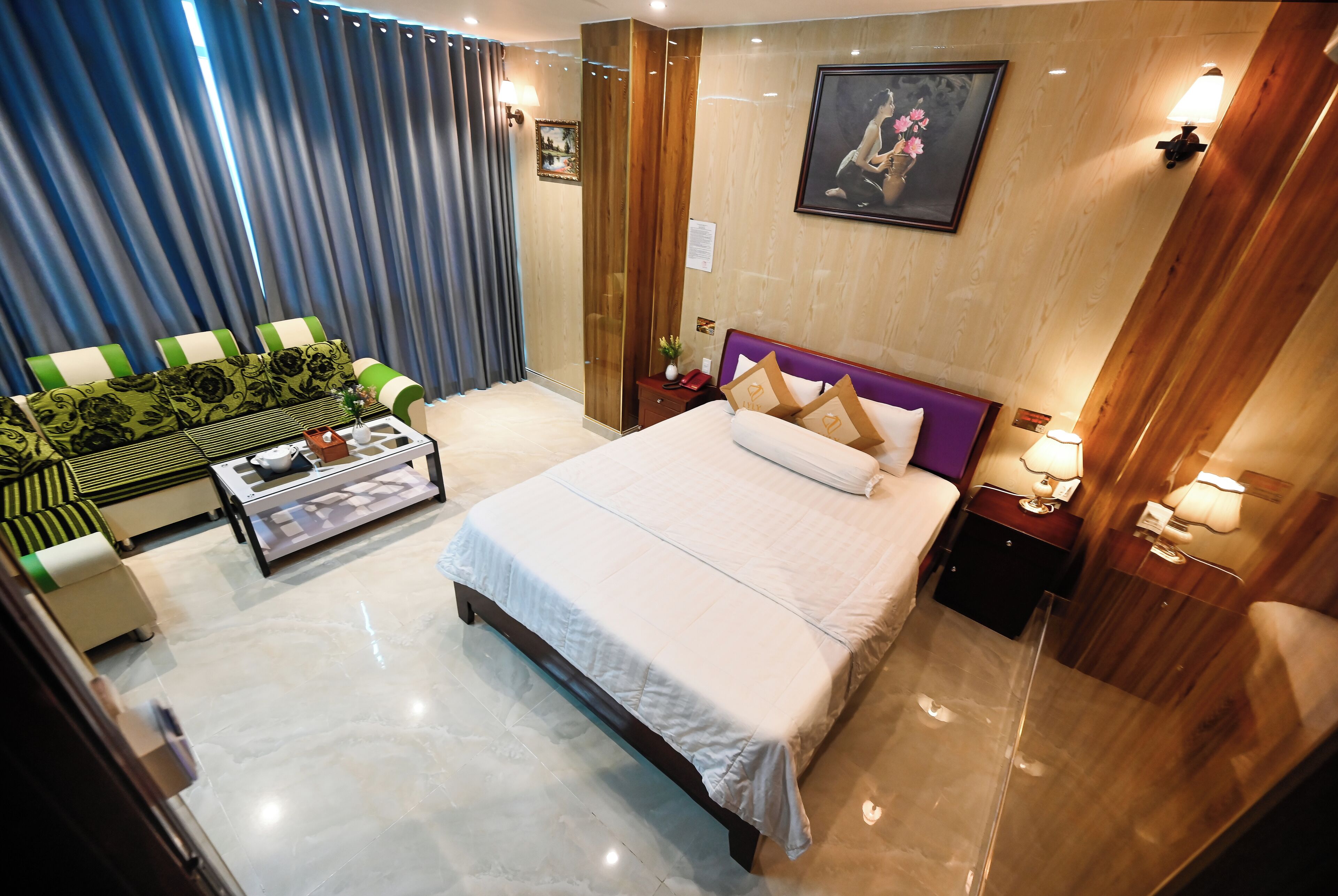 Una habitación de hotel con una cama grande, un sofá con cojines verdes, una mesita de café y una mesita de noche de madera con una lámpara.