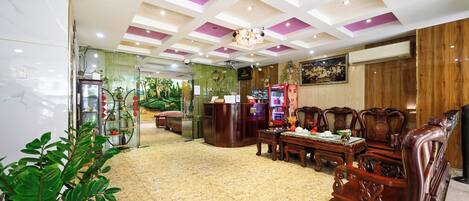 A hotel lobby with a marble floor, wooden furniture, a reception desk, and a green wall with a mural.