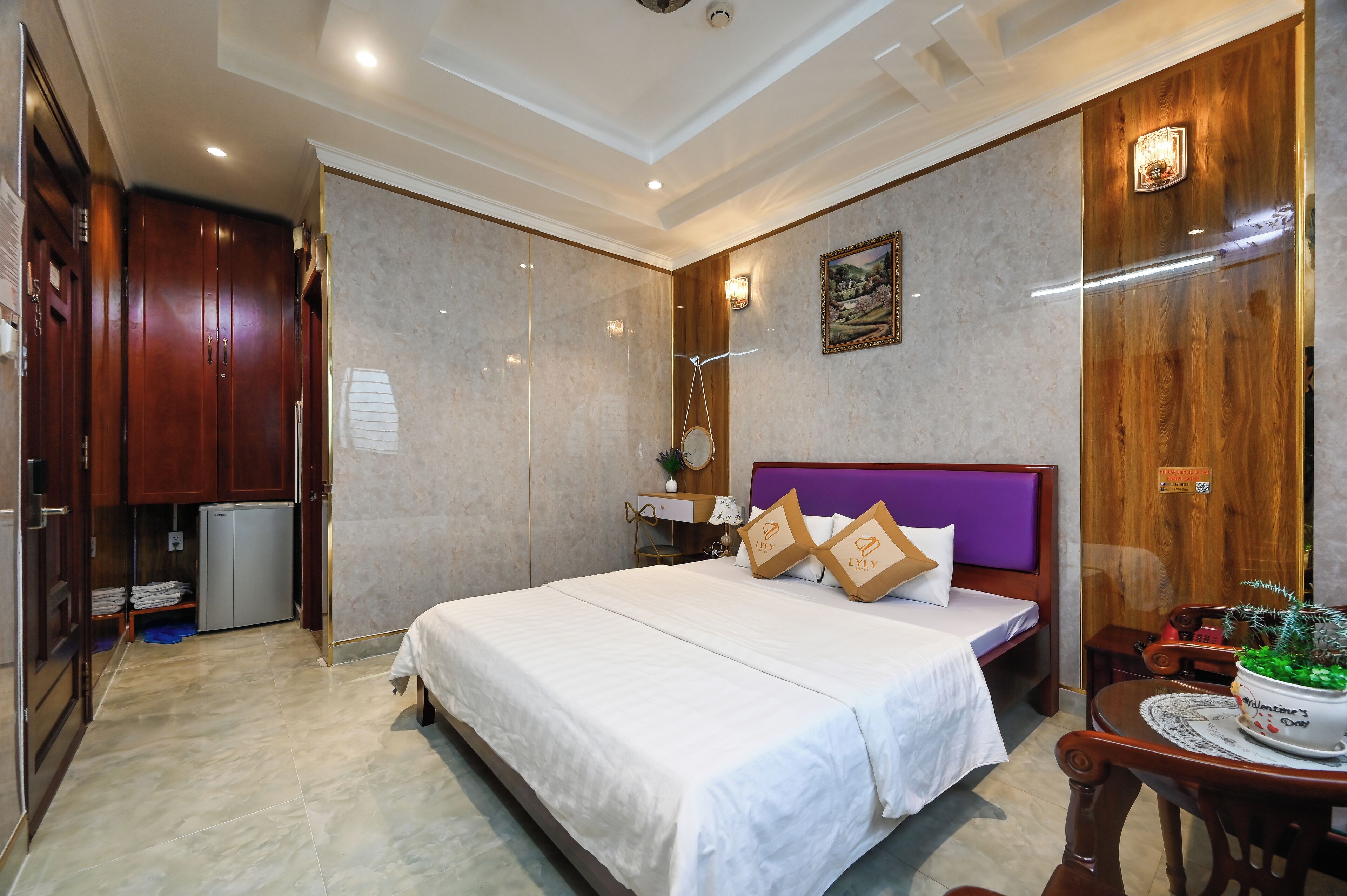 Una habitación de hotel con una cama grande, un armario de madera, un escritorio pequeño y una mesita de noche.