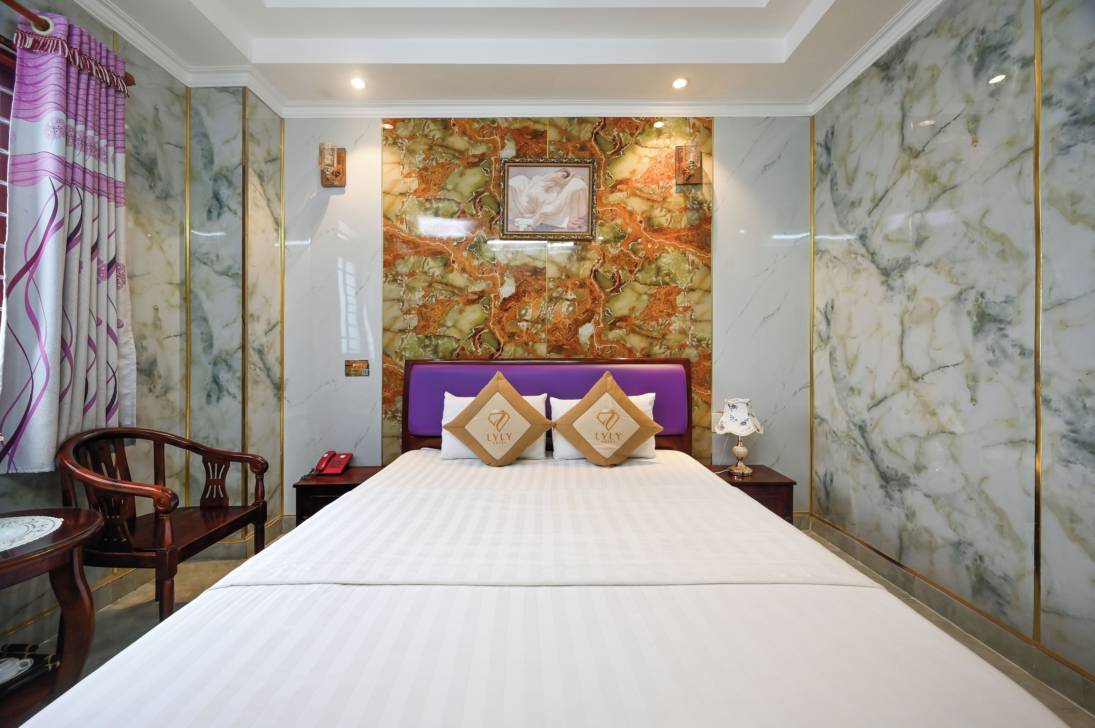 Een hotelkamer met een groot bed, een houten stoel, een klein tafeltje en een nachtkastje met een lamp.