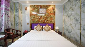 Een hotelkamer met een groot bed, een houten stoel, een klein tafeltje en een nachtkastje met een lamp.