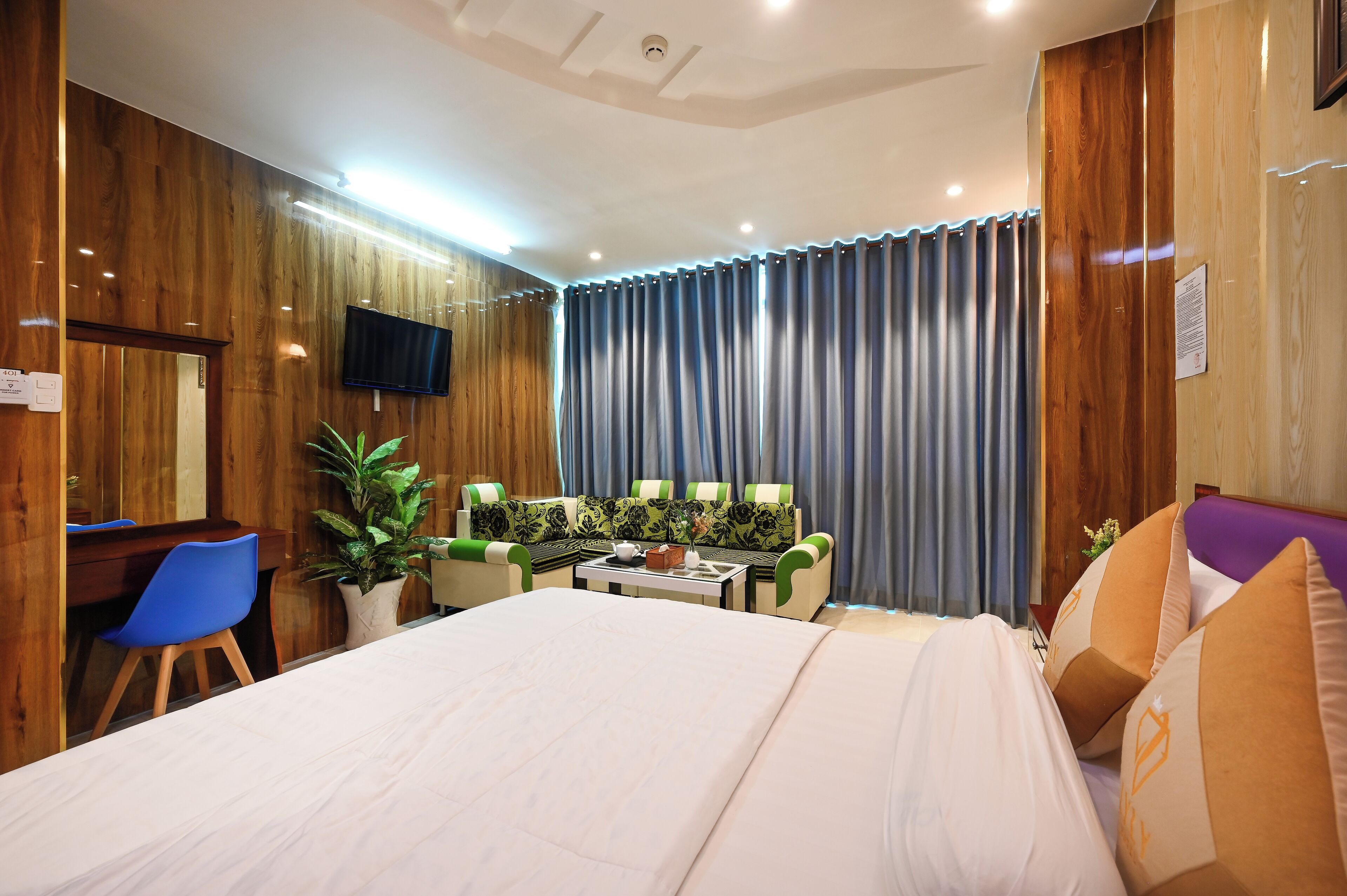 Habitación de hotel con una cama grande, un escritorio con silla, un sofá y un televisor fijado a la pared.