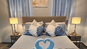 Un letto rifatto con cura, decorato con un cigno realizzato con asciugamani, due lampade ai lati e un quadro appeso alla parete.