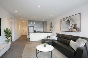 A modern living room with a black leather sofa, a white coffee table, and a large abstract painting on the wall.