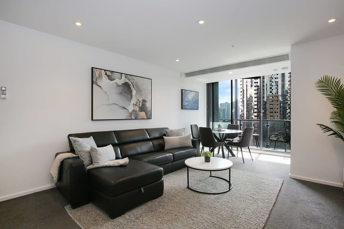 A modern living room with a black leather sofa, a round coffee table, and a large abstract painting on the wall.