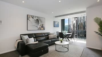 A modern living room with a black leather sofa, a round coffee table, and a large abstract painting on the wall.