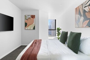A modern bedroom with a large bed, a flat-screen TV, abstract wall art, and a view of a cityscape through a large window. - Southbank 2BR Apt City Views, Free Parking (Southbank)