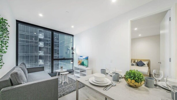 A modern living room with a grey sofa, a small white table, and a large window with a view of buildings.