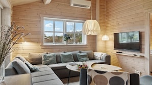 Ein gemütliches Blockhaus-Interieur mit Holzausbau, einem großen Fenster, einer Couch, einem Fernseher und einem Esstisch.