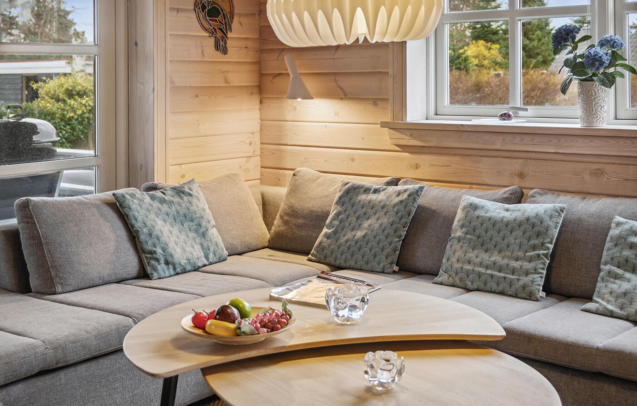 Un salon moderne avec un canapé d’angle, une table basse en bois et un panier de fruits.